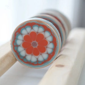 Pu&ograve; includere: Primo piano di diversi saponi rotondi e decorativi con un motivo floreale. I saponi presentano una vivace tavolozza di colori arancione, bianco e turchese. I saponi sono disposti su una superficie di legno chiaro.