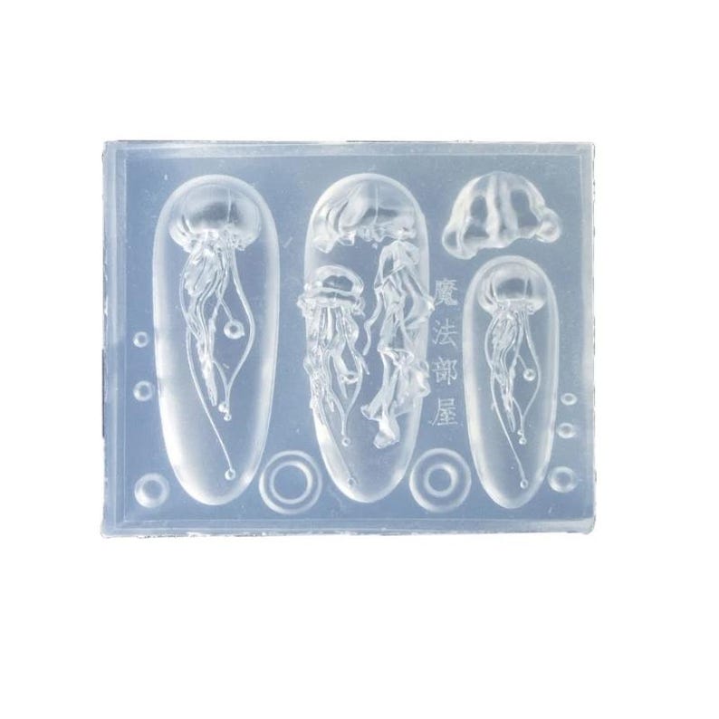 Puede incluir: Un molde de silicona transparente con varios dise&ntilde;os de medusas. El molde incluye formas ovaladas y circulares, con el texto japon&eacute;s "魔法部屋" visible. Las medusas tienen tent&aacute;culos y formas de campana detalladas.