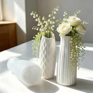 May include: Three white ceramic vases with distinct textures. One vase lies horizontally, while two stand upright, filled with white roses and lily of the valley flowers. The vases feature vertical ribbed and wavy patterns on their exterior surfaces.