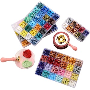 May include: A collection of wax seal supplies, including wax beads in various colors, a wax melting furnace, and wax seal stamps. The wax beads are organized in clear plastic containers. The stamps have pink handles and gold-colored stamp heads.