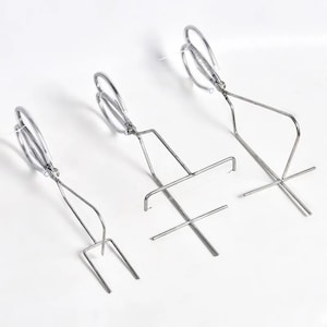 May include: Three silver metal grilling tools. The tools are designed to hold and flip food while grilling. The tools have a long handle and a unique design to hold food securely.