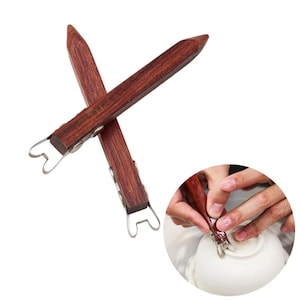 Può includere: Un paio di strumenti in legno per la ceramica con punte in metallo. Gli strumenti sono incrociati e le punte hanno la forma di un cuore. Gli strumenti sono utilizzati per rifinire e modellare la ceramica.