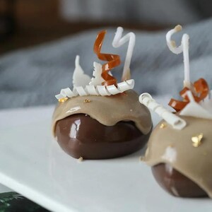 May include: Two chocolate mousse desserts topped with a brown and white swirl, gold leaf, and white chocolate curls.