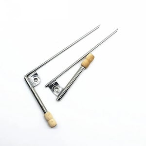 May include: Three metal skewers with wooden handles. The skewers have a pointed end and a small metal bracket. The wooden handles are light brown. The skewers are on a white background.
