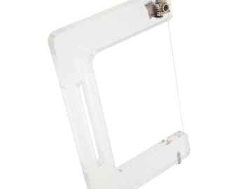 May include: A clear acrylic frame with a wire strung across it. The frame has a knob on the top for adjusting the tension of the wire.