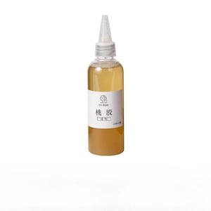 May include: A clear plastic squeeze bottle filled with a light amber liquid. The bottle features a white label with black text including the characters 桃 胶 and 100ml. It has a pointed, translucent nozzle cap for controlled dispensing of the contents.