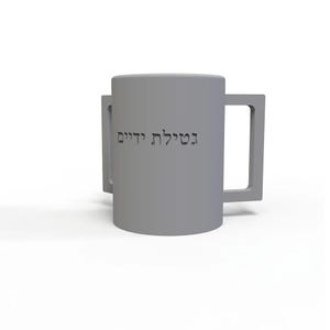 May include: A gray ceramic mug with two square handles. The mug has the Hebrew text "נטילת ידיים" etched into the side. The mug is on a white background.