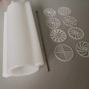 Pu&ograve; includere: Uno stampo in silicone bianco di forma cilindrica e un'asta di metallo, insieme a diversi sottobicchieri decorativi bianchi tagliati al laser con vari motivi geometrici e floreali. I sottobicchieri sono di forma ovale.
