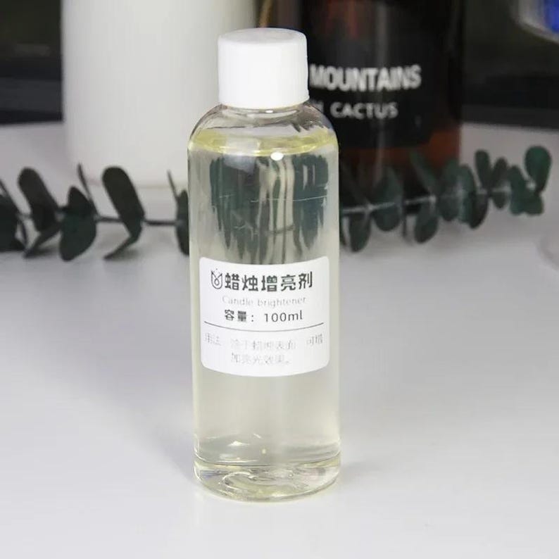 May include: A clear glass bottle with a white cap and a white label. The label says "蜡烛增亮剂" in Chinese and "Candle brightener" in English. The bottle contains a clear liquid and is 100 ml.