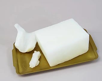 Puede incluir: Un bloque de jabón rectangular blanco en una bandeja dorada con dos formas de jabón blancas más pequeñas.