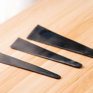 Peut inclure: Trois chausse-pieds noirs de tailles différentes sont disposés en diagonale sur une surface en bois clair. Les chausse-pieds sont faits d'un matériau lisse et solide et ont un design simple et fonctionnel. Le plus petit mesure environ 13 cm.