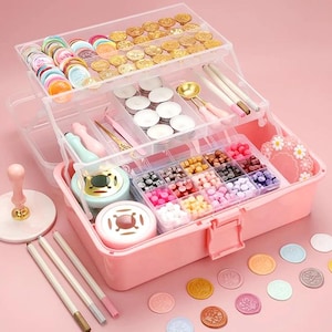 May include: A pink, multi-tiered craft organizer filled with wax seals, wax beads, candles, and tools. The organizer includes a wax seal stamp, pens, and a wax melting pot. Various colors of wax seals and beads are visible.