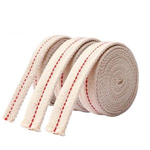 May include: A roll of thick, off-white cotton wick with a red stitched stripe down the center. The wick is tightly wound, with three sections unrolled, showing the red stitching detail. The background is plain white.