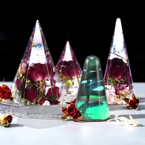 May include: Four clear resin cone-shaped objects, each with a different design. Two cones contain dried red roses, one has a green and blue iridescent pattern, and the last is clear. Dried red roses are scattered around the base.