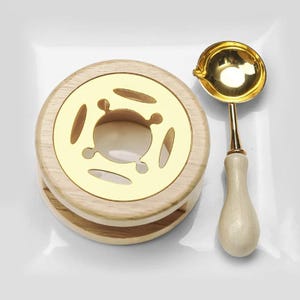 May include: A wooden wax warmer with a gold-colored metal top and a matching gold-colored wax melting spoon. The spoon has a wooden handle. The warmer is round with decorative cutouts.