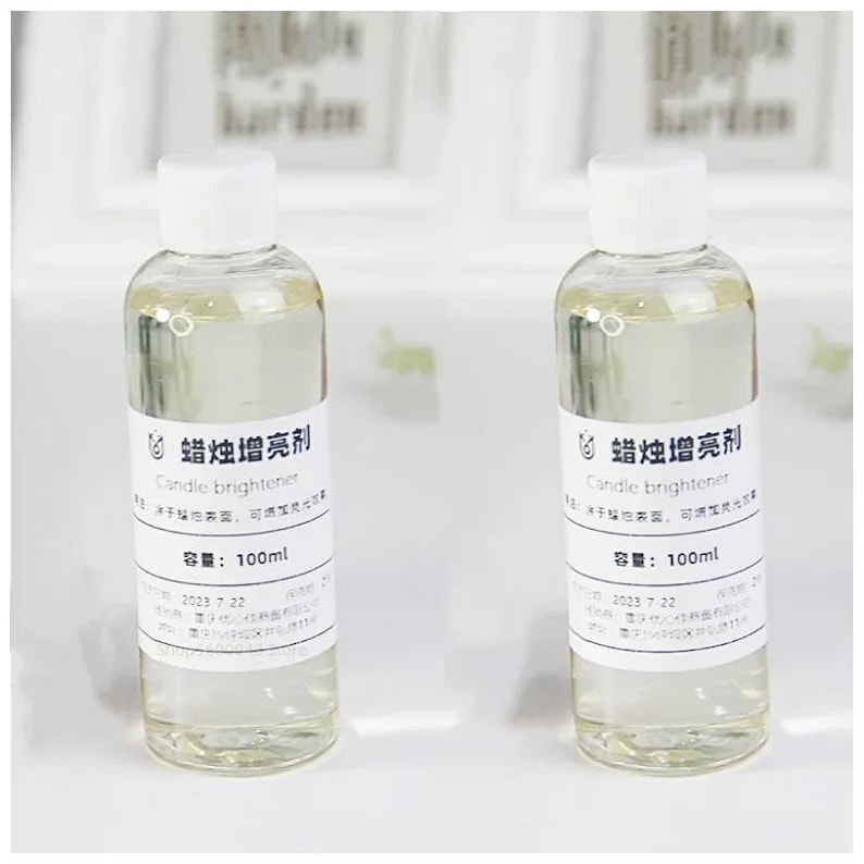 May include: Two clear glass bottles with white labels and white caps. The labels have black text that reads "蜡烛增亮剂 Candle brightener 容量: 100ml 2023 7 22".