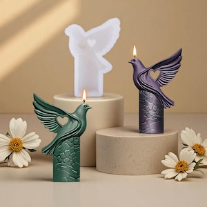 May include: Three dove-shaped candles in white, green, and purple. Each candle features a heart-shaped wing cutout and sits on a textured pedestal. The candles are lit, with flames visible.