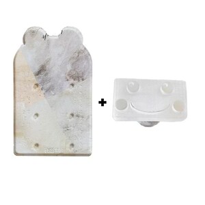 Peut inclure: Un outil rectangulaire clair en forme de jade avec une règle et un dessus en forme d'ours, associé à un petit objet blanc en forme de visage souriant. La règle a des mesures en centimètres. Sur fond blanc.