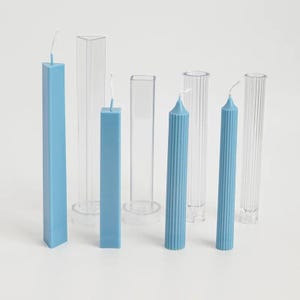 Può includere: Una collezione di candele blu e stampi per candele in plastica trasparente. Le candele hanno varie forme, inclusi design quadrati e scanalati. Gli stampi sono cilindrici e rettangolari, mostrando il processo di fabbricazione delle candele. Le candele sono azzurre.