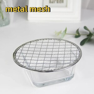May include: A round metal mesh grill sits on top of a clear glass square bowl. The grill is made of thin metal wires and has a silver finish. The bowl is empty.