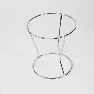 Puede incluir: Un soporte de metal cromado con una parte superior redonda y tres patas. El soporte est&aacute; dise&ntilde;ado para sostener un filtro de caf&eacute;.