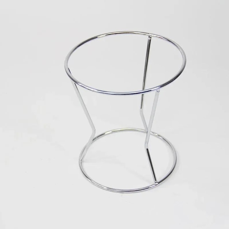 Puede incluir: Un soporte de metal cromado con una parte superior redonda y tres patas. El soporte est&aacute; dise&ntilde;ado para sostener un filtro de caf&eacute;.