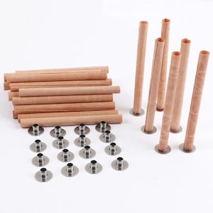 May include: Candle-making supplies, including wooden wicks, metal wick holders, and rolled paper tubes. The wicks are light brown, the holders are silver, and the tubes are a similar colour to the wicks. The items are arranged on a white surface.
