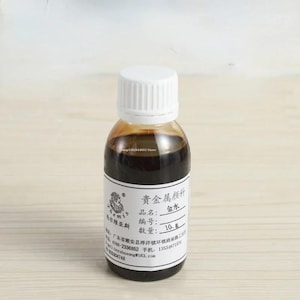 May include: A small, clear plastic bottle filled with a dark brown liquid, topped with a white screw-on cap. The bottle features a white label with black text, including the Chinese characters for precious metal pigment and a quantity of 10 g.