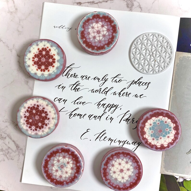 Pu&ograve; includere: Vista dall'alto di sette oggetti decorativi rotondi con intricati motivi geometrici nei toni del bordeaux, bianco e azzurro. Sullo sfondo, un foglio bianco con testo scritto a mano. Citazione di Hemingway.