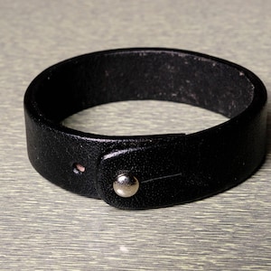 May include: A black leather bracelet with a silver snap closure.