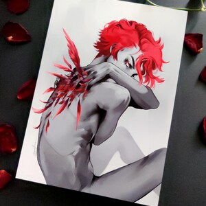 May include: A grayscale art print depicting a figure with red hair and red feather-like details on the back. The figure is seated, arms crossed. Red rose petals are scattered around the print.