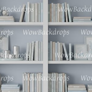 May include: A white bookshelf featuring multiple shelves filled with books in shades of light blue, gray, and white. The shelves also contain decorative items including small vases, framed art, and candles. The text WowBackdrops appears repeatedly.