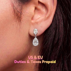 May include: A silver-toned drop earring featuring two clear, pear-shaped faceted stones. The smaller stone is set at the top, connected by a small metal link to a larger, dangling pear-shaped stone below, creating a vertical, articulated design.