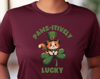 May include: A maroon t-shirt featuring a cartoon cat wearing a green leprechaun hat and sitting on a green shamrock. The text "PAWS-ITIVELY LUCKY" is printed on the shirt.
