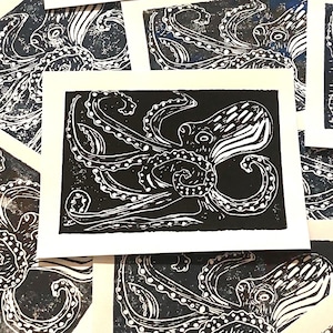 May include: A rectangular art print featuring a high-contrast black and white linocut illustration of an octopus. The design showcases the creature with detailed tentacles and suckers against a solid black background on white paper.