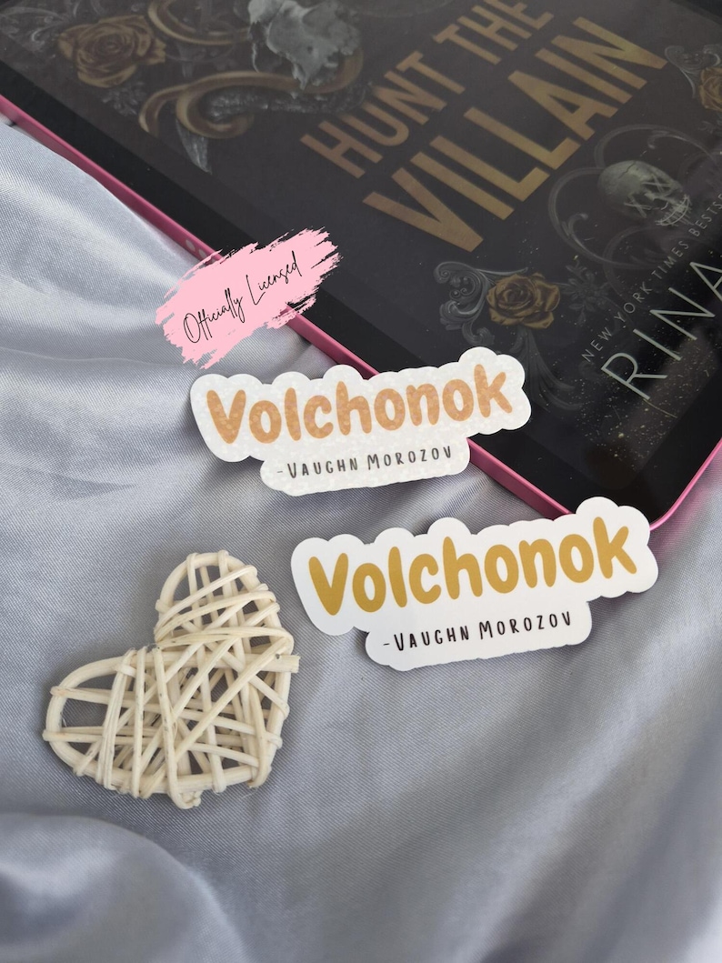 May include: Two stickers with the word "Volchonok" in a playful font, with "-VAUGHN MOROZOV" below. A woven heart and a book titled "HUNT THE VILLAIN" are also visible. The stickers have a light brown and white color scheme.