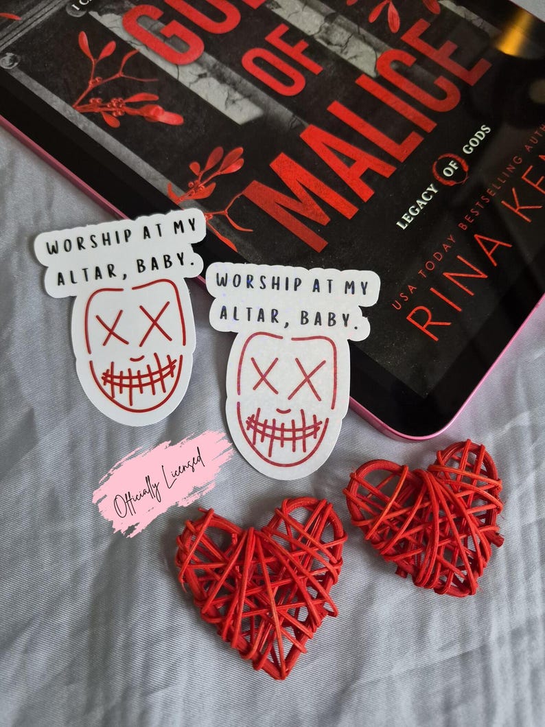 May include: A collection of items including stickers, and heart-shaped decorations. The stickers feature a red and white design with the text "WORSHIP AT MY ALTAR, BABY." Two red woven hearts are also present, along with a book.