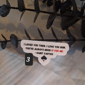 May include: White sticker with black text that reads "I loved you then. I love you now. You've always been it for me. -Saint Carter" with a black spade symbol dripping with black paint. The number 3 is written in black on a white background.