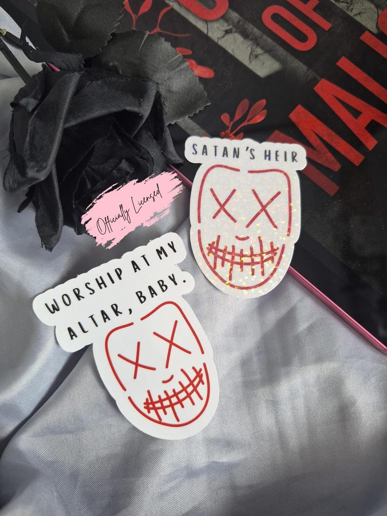 May include: Two white stickers with red outlines and text. One sticker reads "WORSHIP AT MY ALTAR, BABY." and features a face with an "XX" eye design. The other sticker says "SATAN'S HEIR" and has a similar face design.