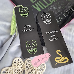 May include: Two black bookmarks with neon green and white graphic designs and text. One bookmark says "Little Monster" and the other says "Volchonok and Mishka". A book titled "Kiss the Villain" is in the background.