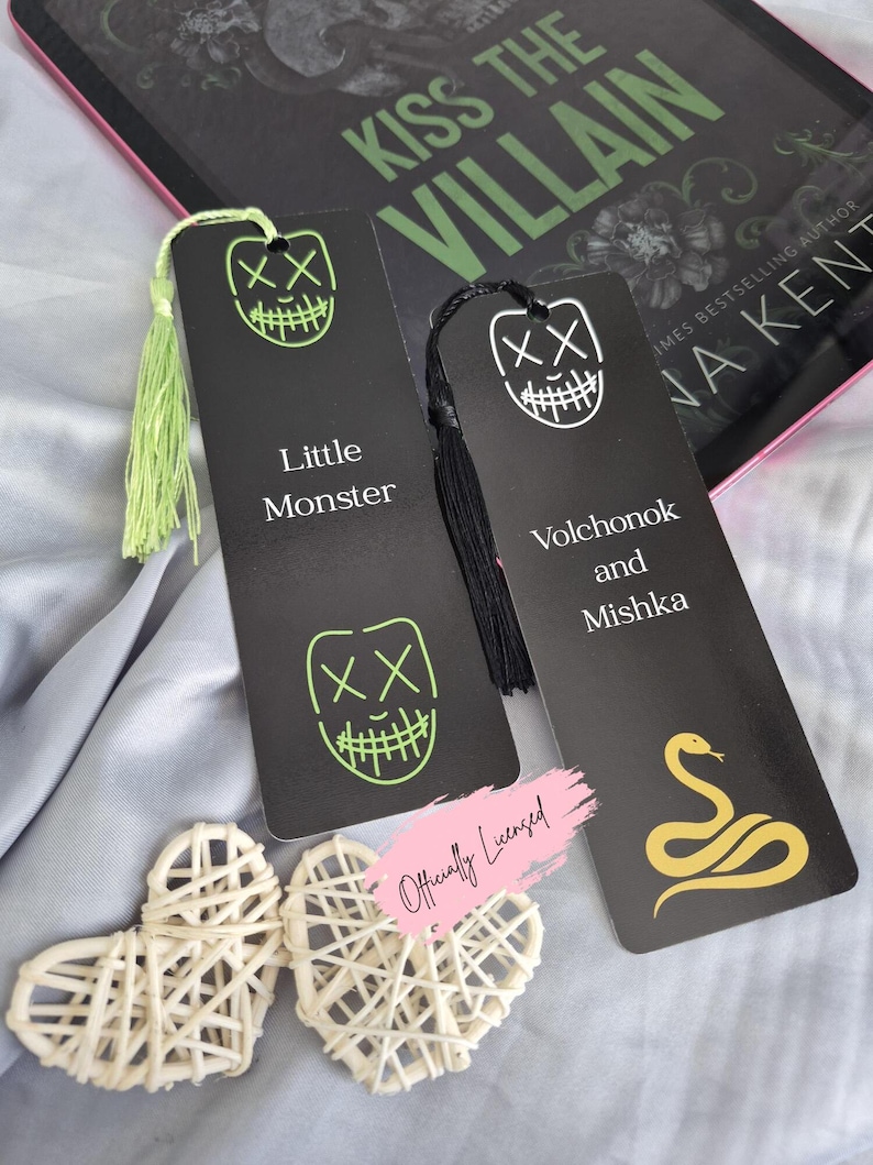May include: Two black bookmarks with neon green and white graphic designs and text. One bookmark says "Little Monster" and the other says "Volchonok and Mishka". A book titled "Kiss the Villain" is in the background.