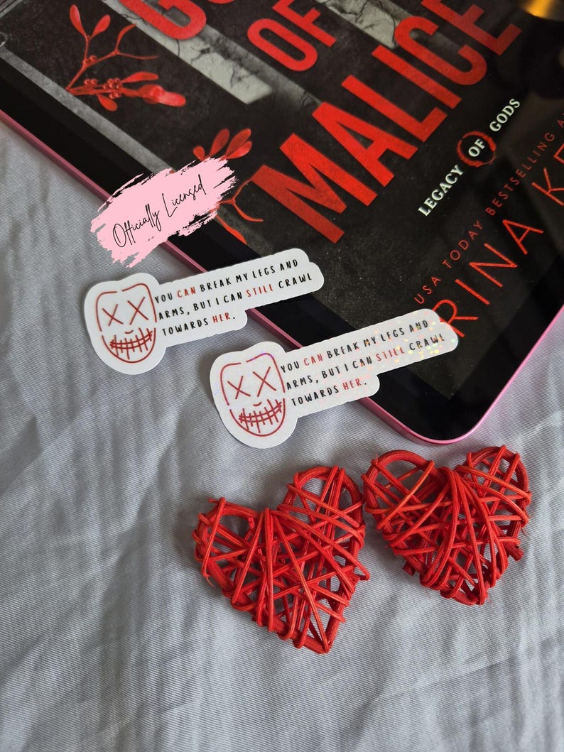 May include: The image features two red woven heart decorations, two stickers with a smiling face design and the text "YOU CAN BREAK MY LEGS AND ARMS, BUT I CAN STILL CRAWL TOWARDS HER.", and a book titled "Legacy of Gods".