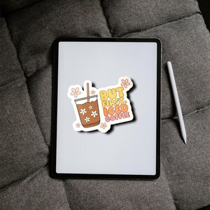May include: A white tablet with a sticker on it that says "BUT FIRST, ICED COFFEE" with a cartoon drawing of a glass of iced coffee with a straw and flowers. The sticker is on a white background with a yellow, orange, and pink gradient.