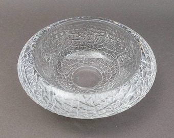 May include: A clear, textured glass bowl with a wide, rounded shape. The bowl's exterior features a detailed, cracked ice pattern, while the interior is smooth. The bowl is designed for decorative or functional use.