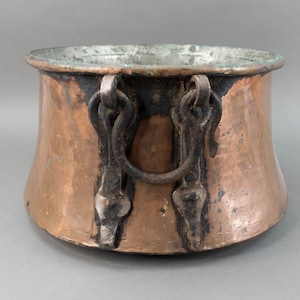Puede incluir: Una olla grande de cobre con dos asas de hierro. La olla tiene un fondo redondeado y una abertura ancha. Las asas están unidas a la olla con remaches de hierro.