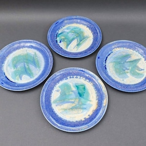 May include: Set of four blue and white ceramic plates with a speckled glaze and abstract green and blue designs.