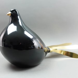 Puede incluir: Una escultura de paloma de cerámica negra con cola dorada. La paloma tiene un acabado brillante y una forma realista.