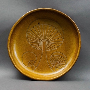 May include: A brown ceramic serving dish with a raised design of three mushrooms. The dish has a slightly scalloped edge.