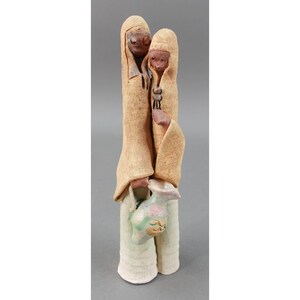 May include: A ceramic sculpture of two figures wearing robes, one holding a pitcher. The figures are made of brown clay and have a rustic, hand-crafted look.