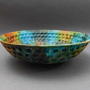 Puede incluir: Un cuenco grande de cerámica con una superficie texturizada y un patrón. El cuenco está decorado con tonos de azul, verde, marrón y naranja.